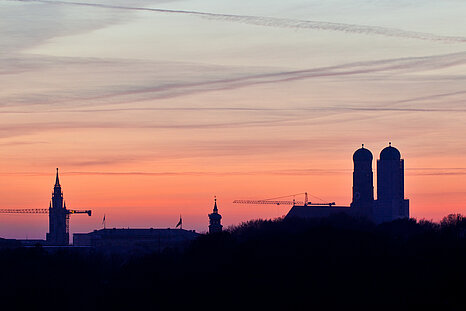 Zu sehen ist ein rosa-roter Sonnenuntergang und die Münchner Skyline