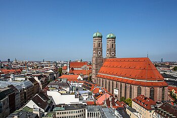 Zu sehen ist die Aussicht über die Dächer von München mit der Frauenkirche rechts im Bild
